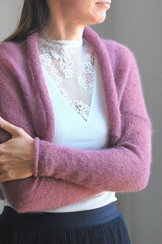 a woman wearing a pink cardigan and black pleated skirt with her arms crossed