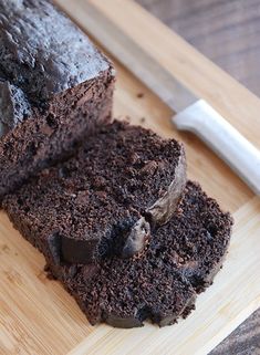 a loaf of chocolate cake on a cutting board with a knife next to it,