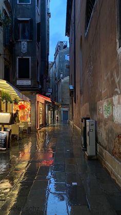 an alley way with tables and chairs on the sidewalk in the rain at night time