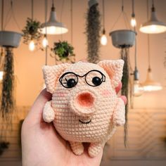 a hand holding a small crocheted pig with glasses on it's face