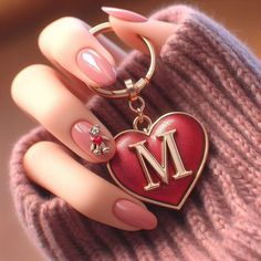 a close up of a person holding a heart shaped keychain with the letter m on it