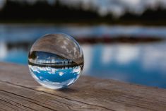 a glass ball sitting on top of a wooden table next to a body of water