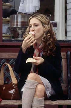 a woman sitting on a wooden bench eating food with her legs crossed and wearing knee high socks