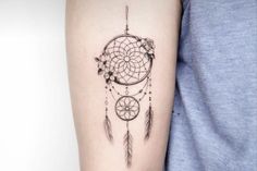 a woman's arm with a tattoo that has a small dream catcher on it