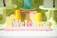 there is a welcome sign made out of plastic cups and lemons on the table