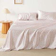 a bed with pink sheets and pillows in a white room next to a lamp on a table