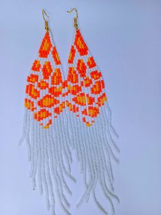 two pairs of orange and white beaded earrings with long fringes on top of each ear