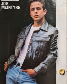 a young man wearing a leather jacket leaning against a door with his hands in his pockets