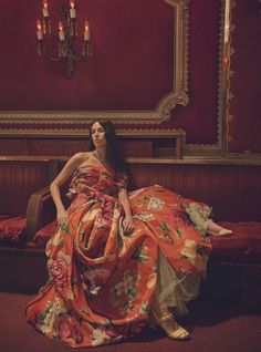 a woman sitting on top of a bed in a room with red walls and chandeliers