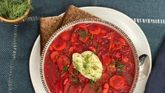 a white plate topped with a red vegetable soup next to a bowl of sour cream