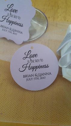 two wedding tags on a table next to a wine glass and bottle stopper with the words love is the new happiness printed on it