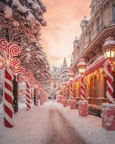 candy canes are lined up on the sidewalk in front of buildings and trees covered with snow