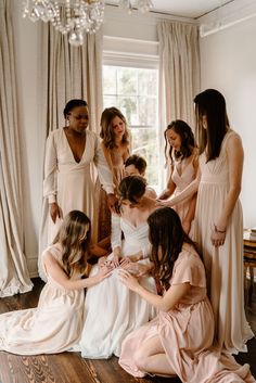 a group of women standing around each other in front of a window with one woman tying the bride's dress