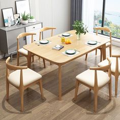 a wooden table with white chairs and plates on it in front of a large window