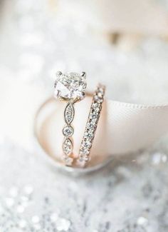 an engagement ring and wedding band sitting on top of a white cloth with sparkle in the background