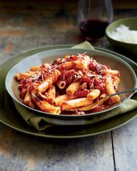 pasta with sauce and cheese in a bowl on a table next to a glass of wine