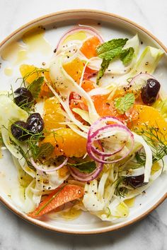 a white plate topped with salad and oranges on top of a marble countertop