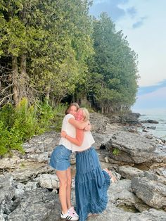 two people hugging each other while standing on rocks near the water