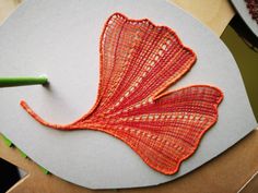 an orange piece of string art sitting on top of a white plate next to a green pencil