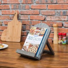 a cookbook is sitting on a wooden table next to a plate of food and a cutting board