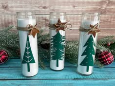 three christmas candles sitting next to each other on top of a blue wooden table with pine trees