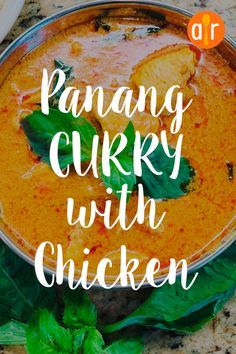 a pan filled with curry and chicken on top of a counter next to green leaves