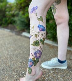 a person with tattoos on their legs is standing in front of some bushes and flowers