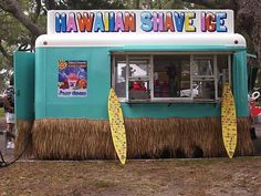 a blue and white ice cream stand with yellow surfboards on the outside, in front of some trees