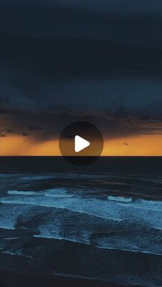 the sun is setting over the ocean with dark clouds