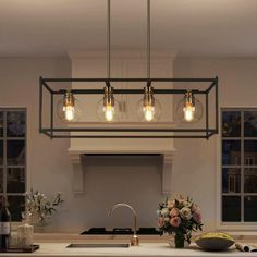 a kitchen island with lights hanging from it's ceiling and flowers on the counter