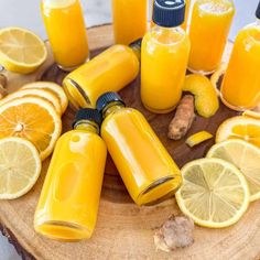 orange juice in glass bottles surrounded by sliced lemons and ginger on a wooden board