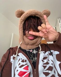 a person with dreadlocks wearing a brown bear hoodie and making the peace sign