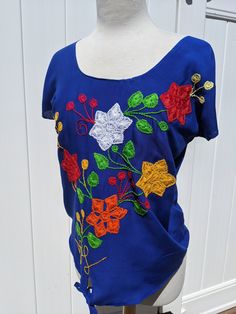 Blue blouse with beautiful hand embroidered colorful flowers.  Made of Rayon- the best fabric for summer wear. L: 25" W: 20' Oh Tierra del Sol's items are unique and handmade by artisans from Oaxaca, Mexico.  Care recommendations: **Wash by hand - be extra careful in the embroidery area of the garment ** Hang Dry in the shade Folk Style Embroidered Top For Fiesta With Floral Embroidery, Folk Style Embroidered Top With Floral Embroidery For Fiesta, Folk Style Floral Embroidered Top For Fiesta, Cinco De Mayo Fiesta Blouse With Floral Embroidery, Cinco De Mayo Floral Embroidery Blouse, Fiesta Cotton Top With Floral Embroidery, Cotton Floral Embroidered Top For Fiesta, Floral Embroidered Cotton Top For Fiesta, Folk Style Embroidered Cotton Top For Fiesta