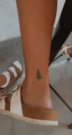 a woman's foot with a small pine tree tattoo on her left side ankle