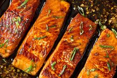 four pieces of cooked salmon sitting on top of a pan covered in sauce and herbs