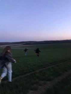 three people are running through the grass with kites in the sky behind them and one person is flying a kite