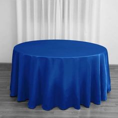 a round table with a blue cloth on it in front of a white wall and wooden floor