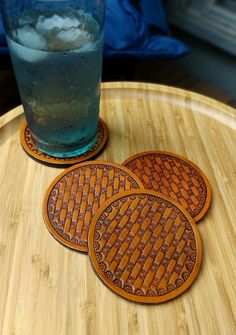 three coasters sitting on top of a wooden table next to a glass filled with water