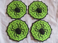 four green and black spider web coasters on a white sheet