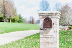 a brick mailbox in the middle of a grassy area with trees and grass behind it