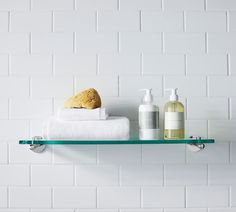 towels and soaps are sitting on a glass shelf in front of a white brick wall