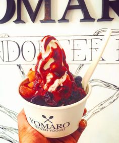 a person holding up a ice cream sundae in front of a sign that says yogurt shop