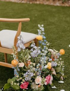 a wooden chair sitting on top of a lush green field next to flowers and greenery