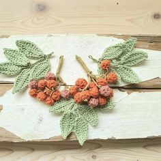 crocheted flowers and leaves hang from hooks on a piece of white painted wood