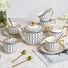 a white and blue tea set with gold trimmings on the rim, sitting on a lace tablecloth