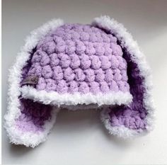 a purple and white crocheted hat on a white surface with one ear flap open