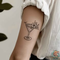 a woman's arm with a tattoo that has a martini glass and flowers on it