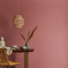 a room with pink walls and a wicker chair next to a small wooden table