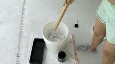 a woman is painting the floor with white paint and a wooden spatula in her hand