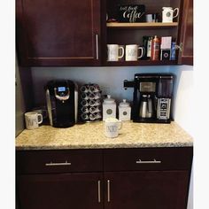 a kitchen counter with coffee maker, cups and other items sitting on top of it